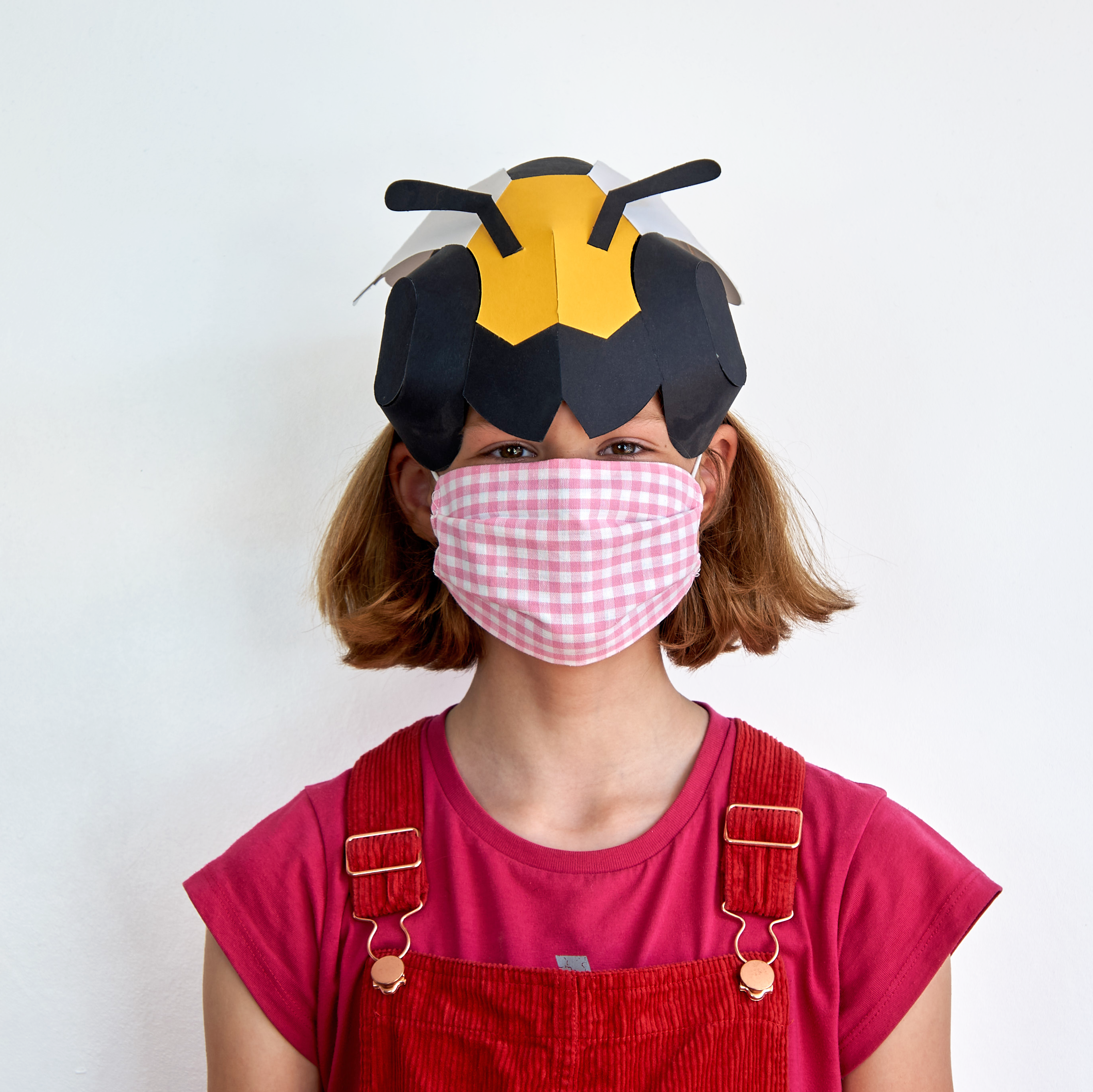 Person wearing a bee hat and pink checkered mask on a white background