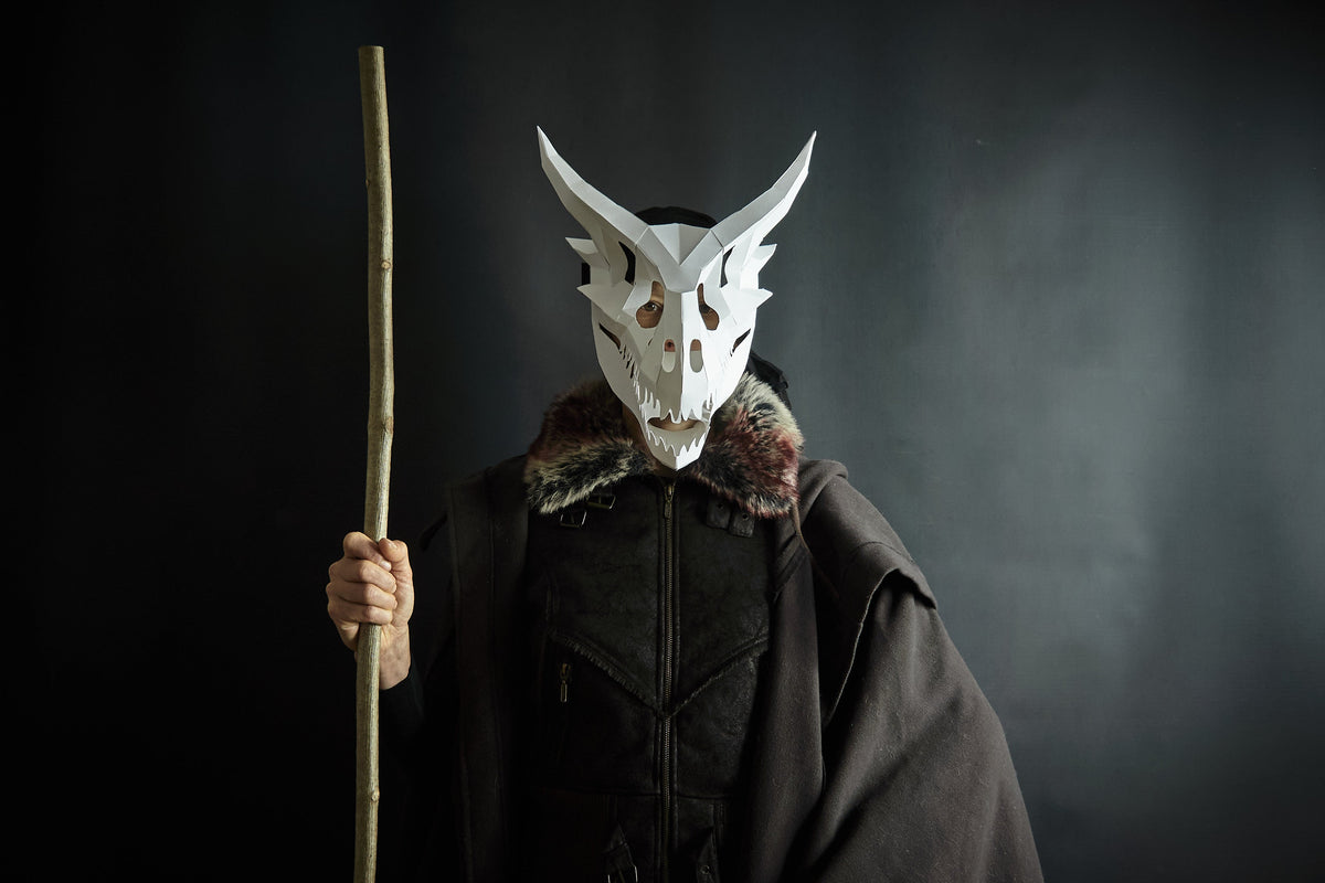Person wearing a cardboard dragon skull mask and holding a staff in a dark setting