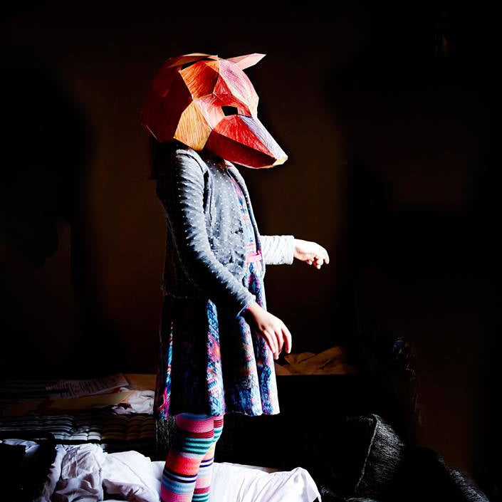 Person wearing a fox mask in a dark room with colorful striped leggings.