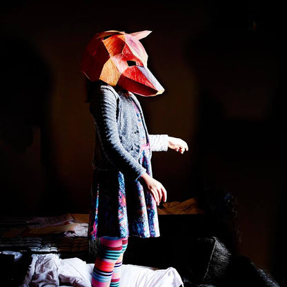 Person wearing a fox mask in a dark room with colorful striped leggings.